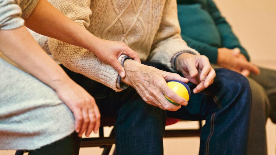 Loneliness in the Caring Professions: Finding Connection & Purpose for Nurses and Care Workers 5 An elderly person receives support from a caregiver, holding hands indoors, showcasing compassion.
