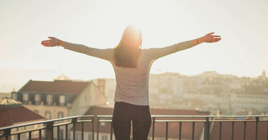 Affordable Life Coaching — A Gentle, Meaningful Approach to Personal Growth 3 A woman stands with outstretched arms on a sunny balcony, embracing the morning light.