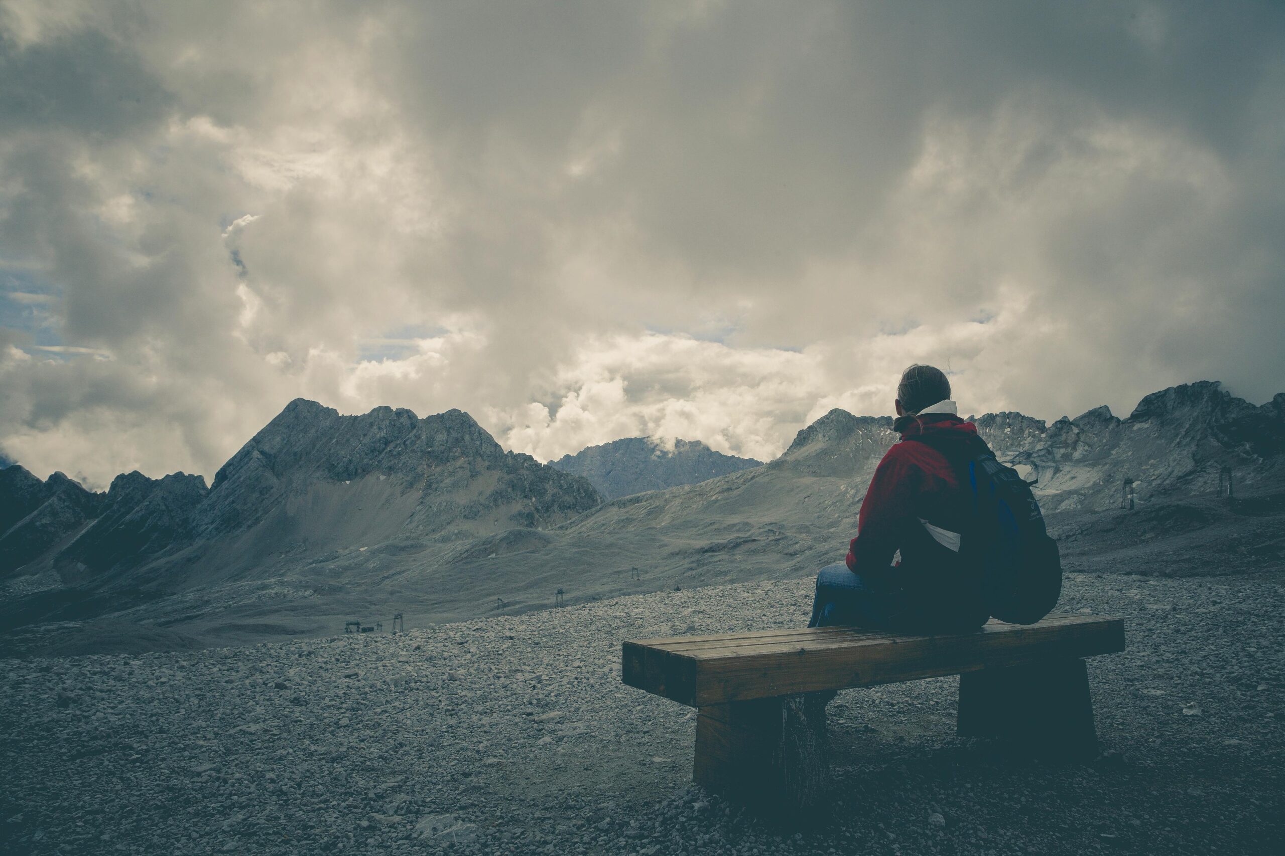 Why Do I Feel So Disconnected From Everyone? 2 A solitary traveler sits on a bench, gazing at a mountain range under a cloudy sky.
