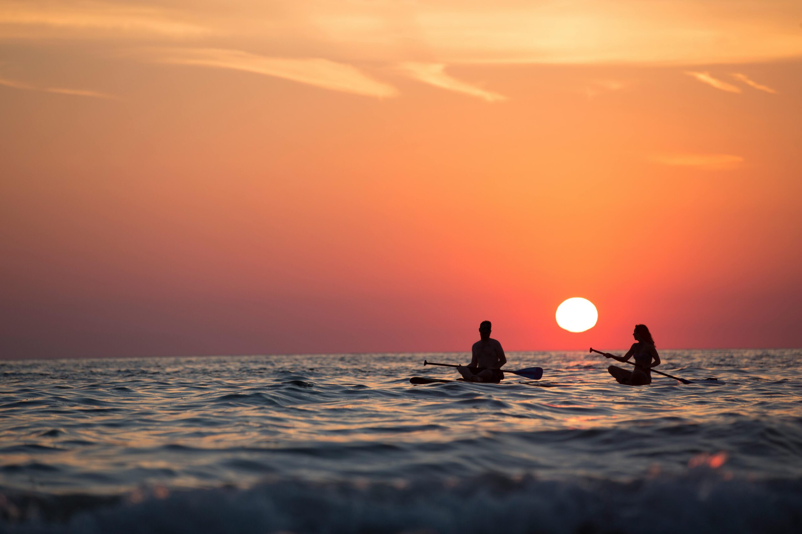 Why Do I Feel Lonely in My Relationship? 5 Silhouette of a couple paddleboarding on the ocean during a stunning sunset, capturing romance and adventure.