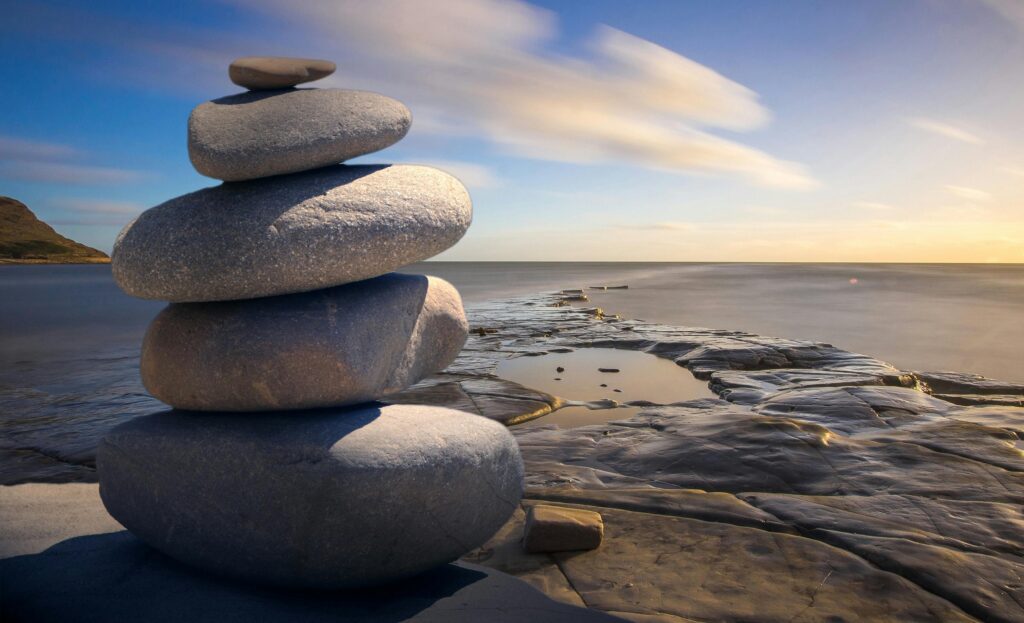 How To Create Positive Habits And A Positive Mindset With Mindfulness 7 A serene stack of stones on the rocky seashore during a peaceful sunrise, embodying balance and zen.