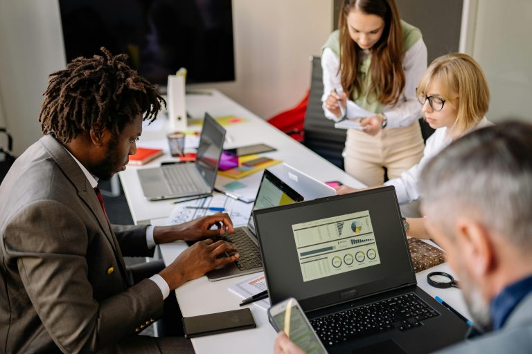 Diverse coworkers engaged in teamwork using laptops and digital devices in a modern office setting.